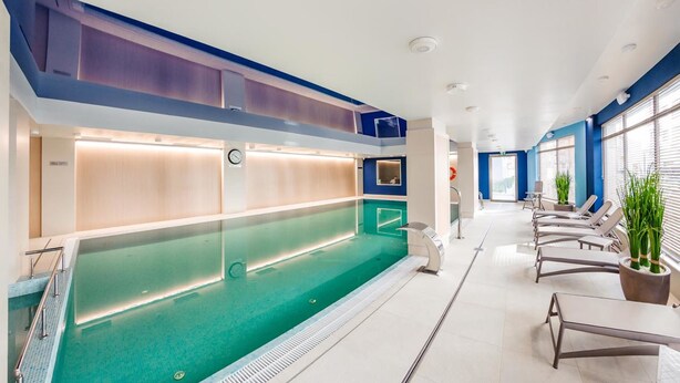 A modern indoor swimming pool with a long, narrow design, surrounded by lounge chairs and potted plants. - City Center Apartments SPA & Wellness by Apartmore (Gdansk)