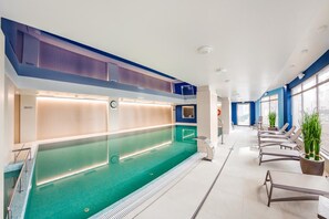 A modern indoor swimming pool with a long, narrow design, surrounded by lounge chairs and potted plants. - City Center Apartments SPA & Wellness by Apartmore (Gdansk)