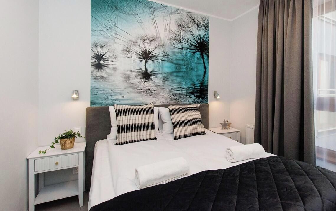 A modern hotel room with a large abstract painting, a black quilted bedspread, and a view of the city through the window.