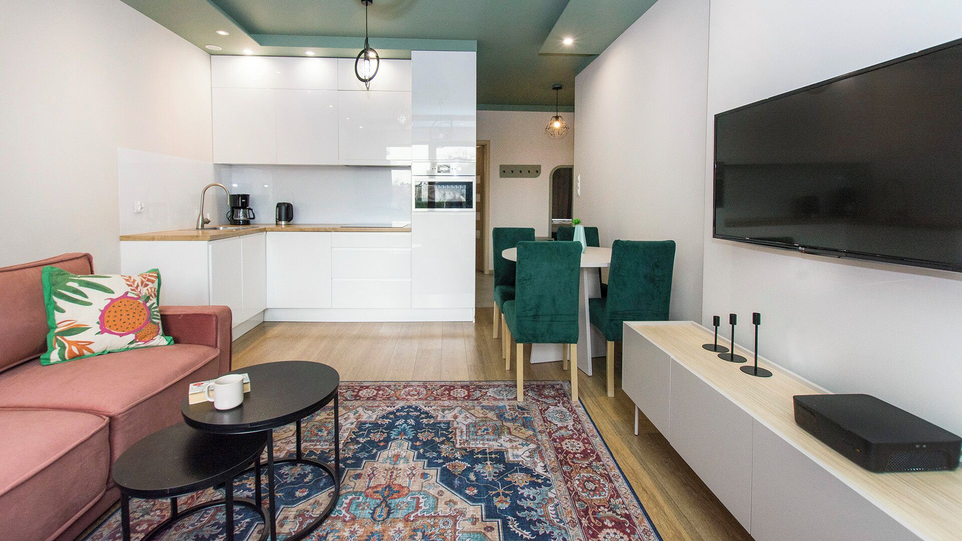 Un espace de vie moderne comprenant un canapé, une table basse, un tapis, un coin repas, une cuisine et un téléviseur.