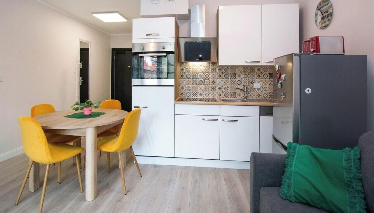 A compact kitchen with a dining table, chairs, and a refrigerator.