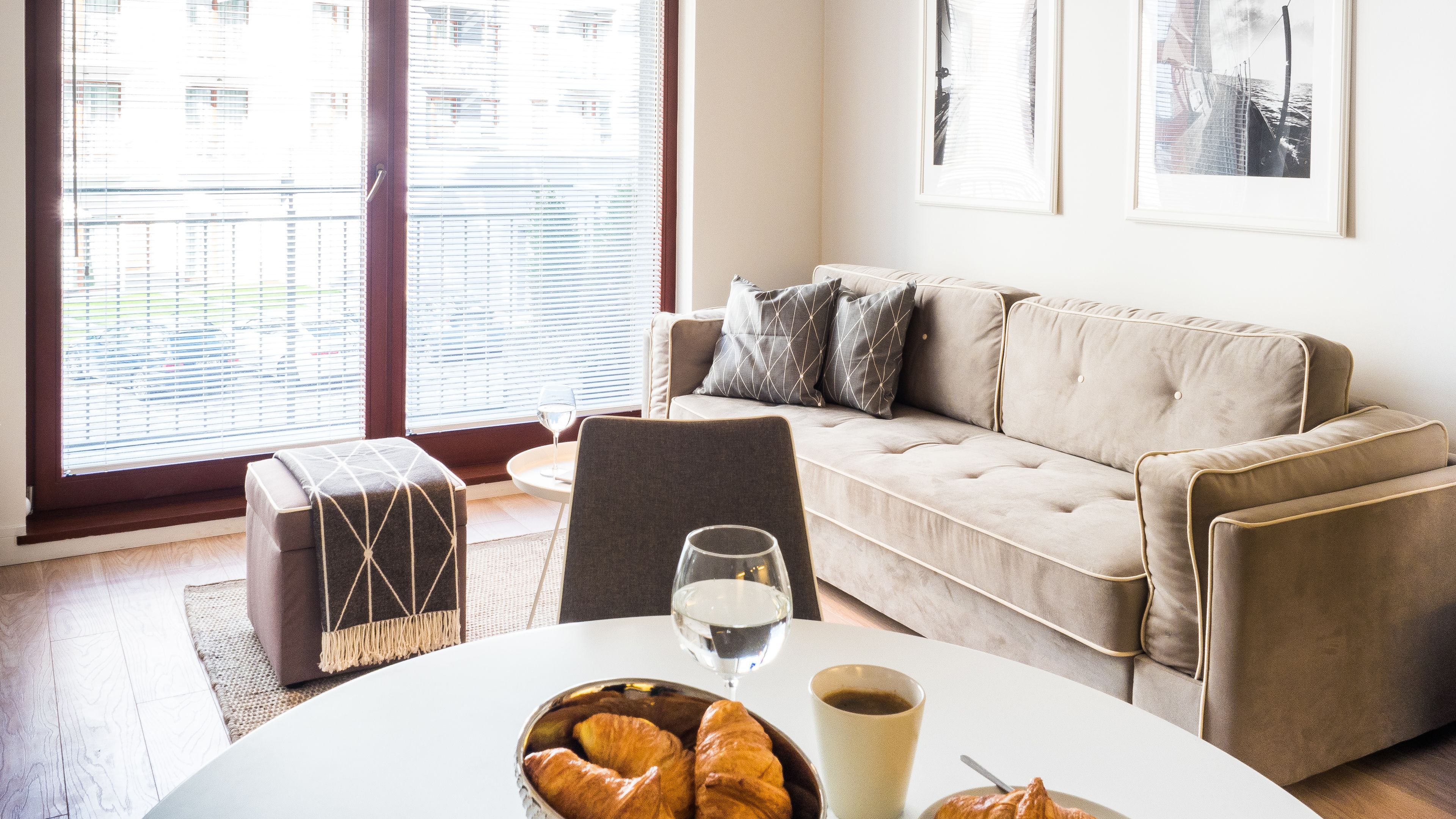 A living room with a sofa, ottoman, and a table with croissants and drinks.