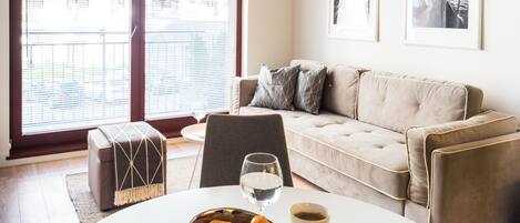 A living room with a sofa, ottoman, and a table with croissants and drinks.