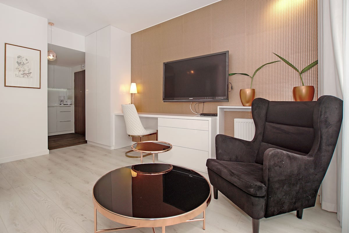 A modern living room with a flat-screen TV, a dark armchair, a round coffee table, and a white sofa.