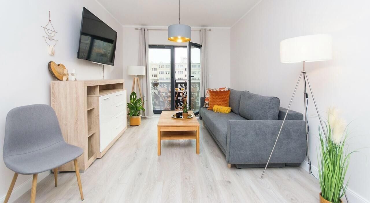 A modern living room with a grey sofa, a wooden coffee table, a grey armchair, a TV mounted on the wall, and a floor lamp.