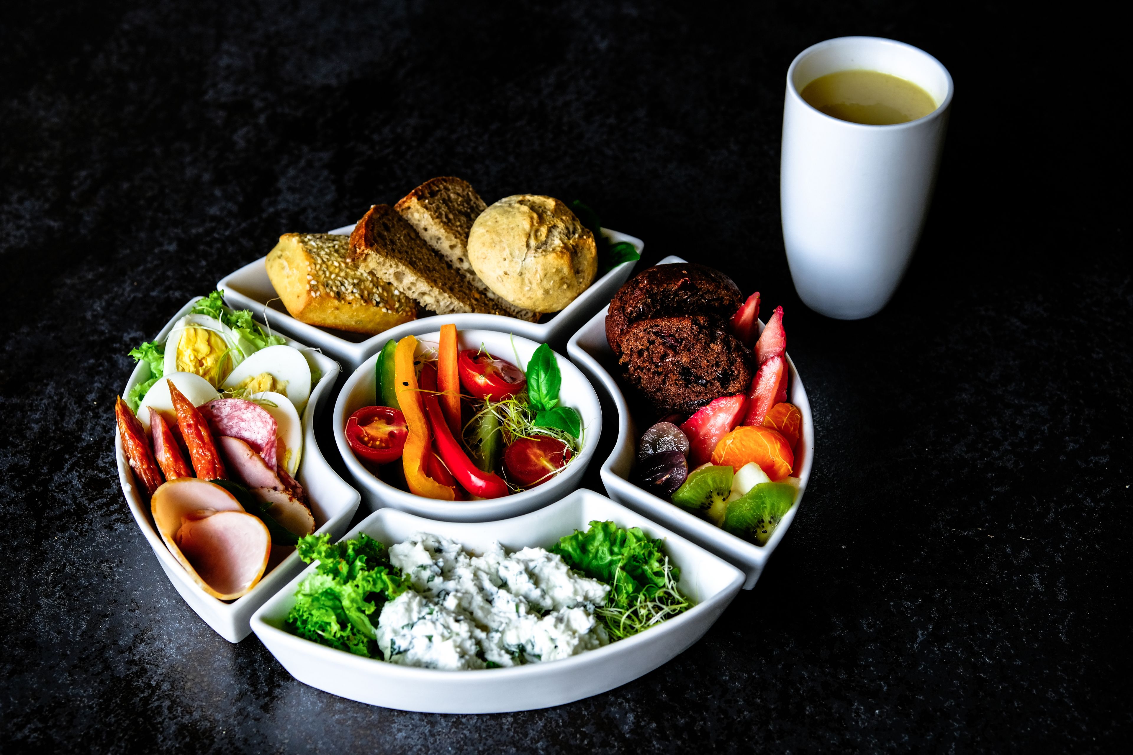A variety of food items arranged on a white plate, including meats, vegetables, and a cup of coffee.