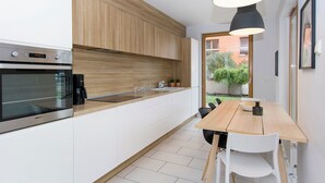 A modern kitchen with wooden cabinets, a built-in oven, and a dining area with a wooden table and chairs. - City Center Apartments SPA & Wellness by Apartmore (Gdansk)