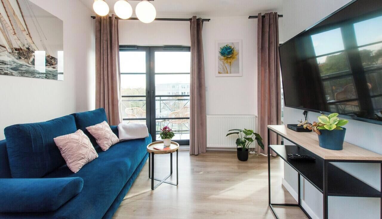 A modern living room with a blue sofa, a small round table, a flat-screen TV, and a potted plant.