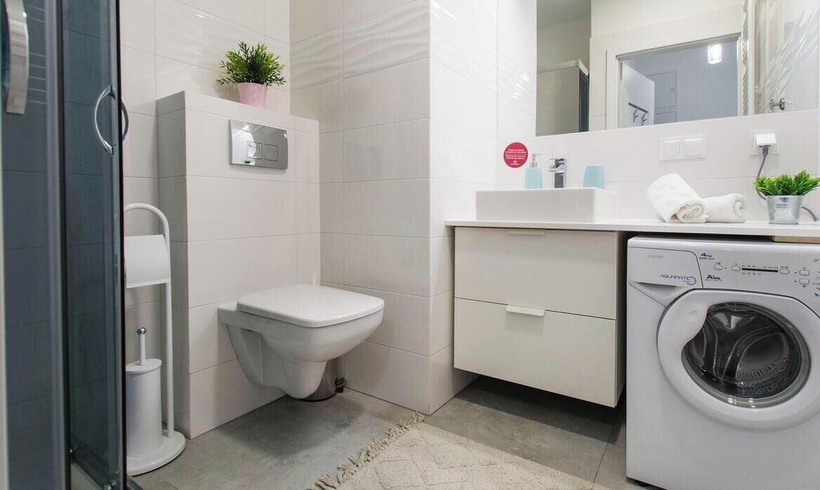 Une salle de bain moderne équipée de toilettes, d’un lavabo, d’un miroir et d’un lave-linge.