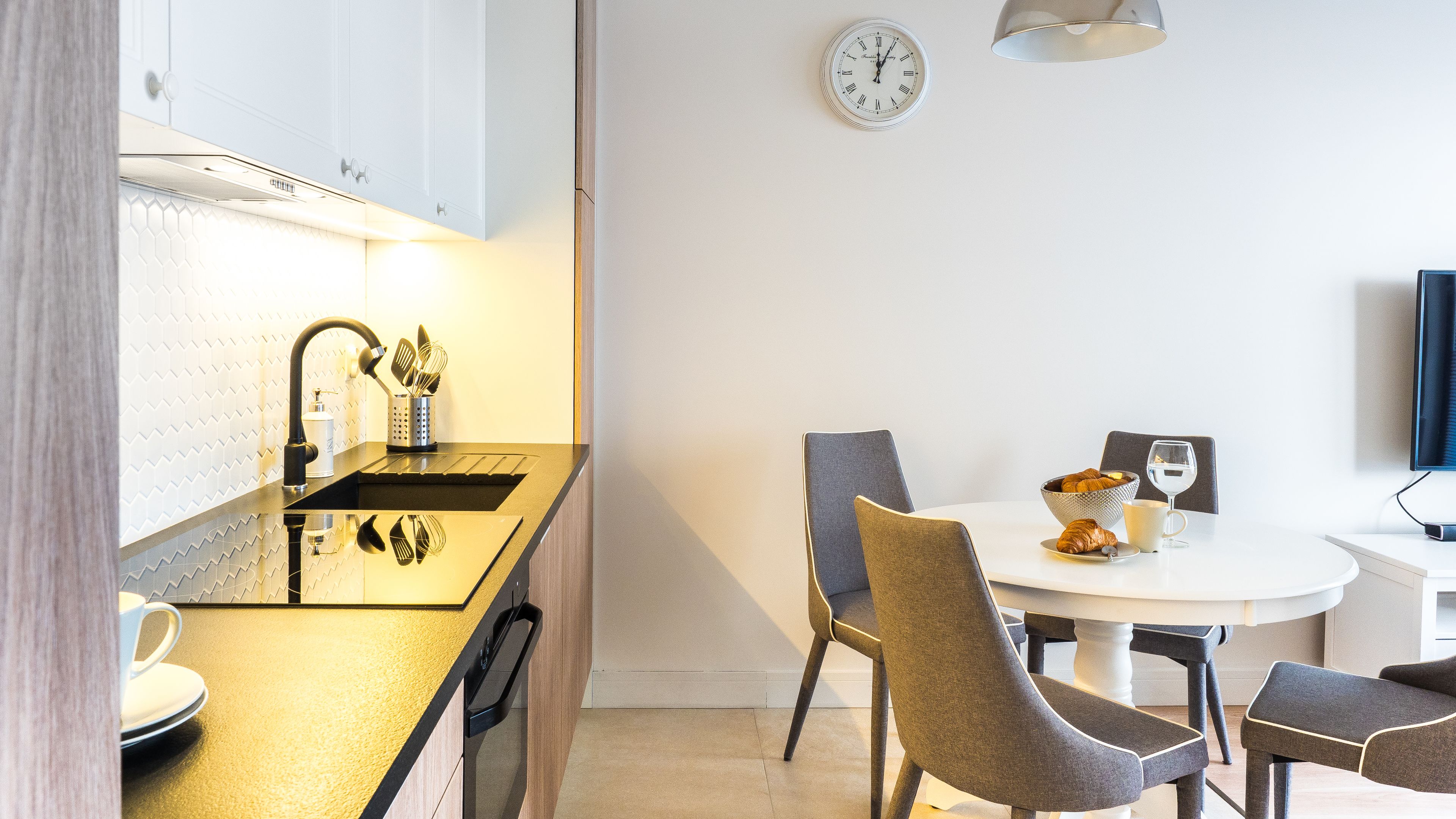 Una cocina moderna con encimera negra, electrodomésticos de acero inoxidable y zona de comedor con una mesa redonda y sillas.