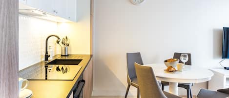 Una cocina moderna con encimera negra, electrodomésticos de acero inoxidable y zona de comedor con una mesa redonda y sillas.