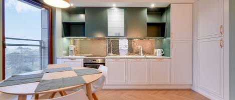 A modern kitchen with white cabinets, a wooden herringbone floor, and a large window overlooking a cityscape.