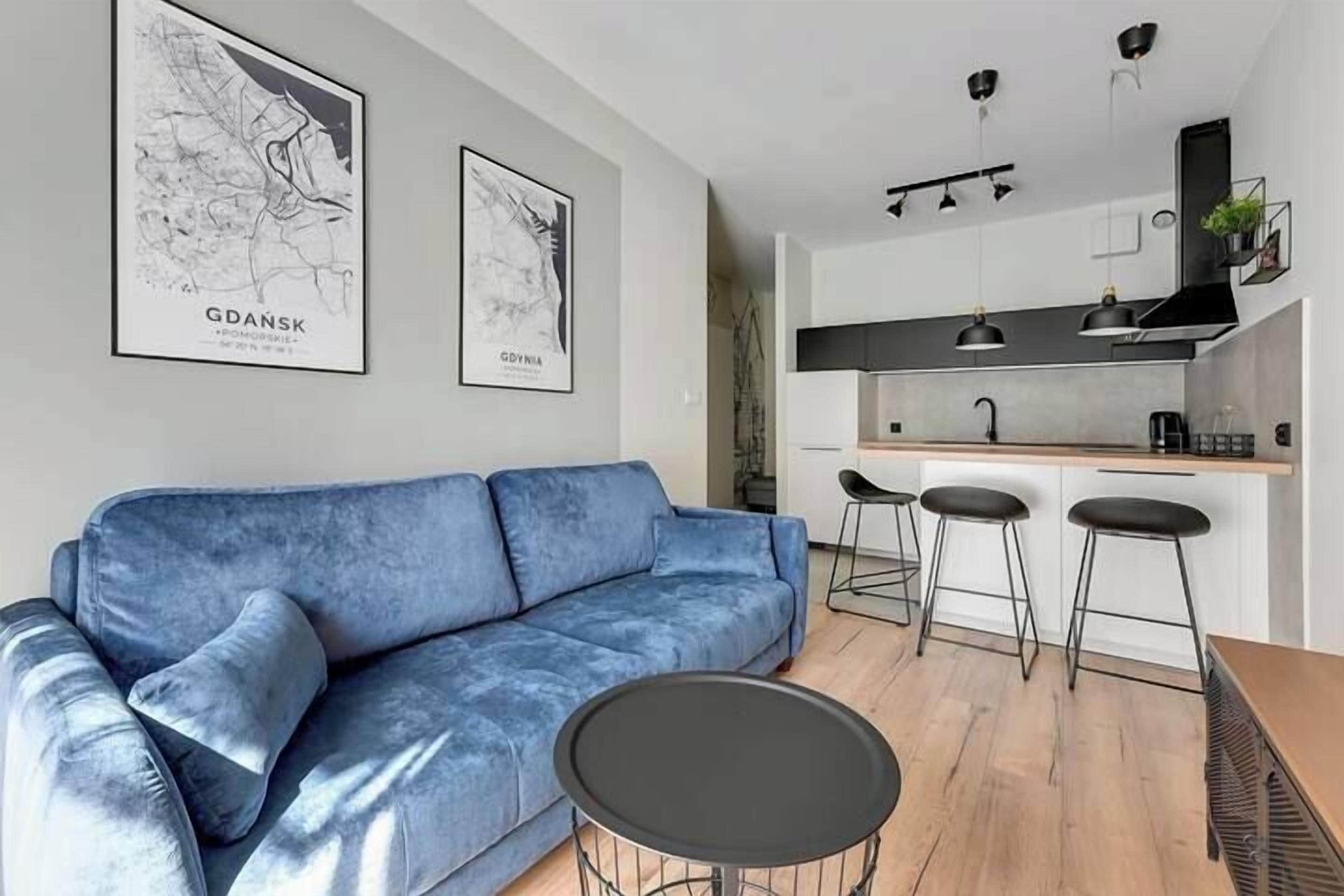 Una sala de estar moderna con un sofá azul, una mesa redonda y una cocina con taburetes de bar.