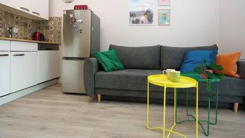 Eine moderne Küche mit weißen Schränken, einem grauen Sofa und einem gelben Tisch mit einer Zimmerpflanze.