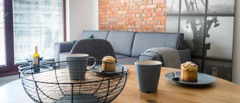 Un salón moderno con pared de ladrillo, un sofá gris, una mesa de centro con cesta de mimbre y una ventana con persianas.