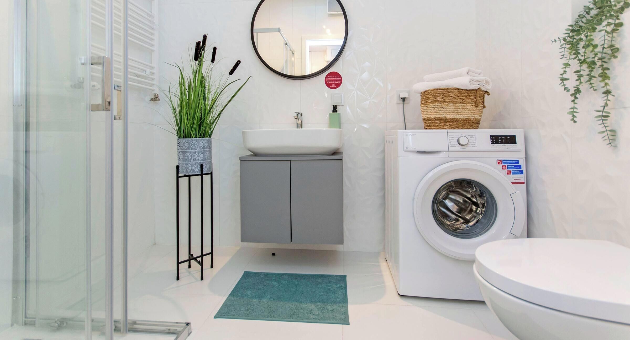 A modern bathroom with a glass shower enclosure, a sink with a mirror, a washing machine, and a toilet.