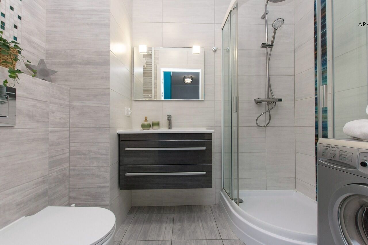 Ein modernes Badezimmer mit Toilette, Waschbecken mit Spiegel, Dusche und Waschmaschine.