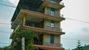 A multi-story hotel with balconies, a sign indicating it is a hotel, and a view of the surrounding area. - Hotel Young's Stupa (Lekhnath)