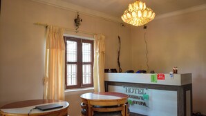 A hotel reception desk with a sign reading "HOTEL YOUNG'S STUPA". There is a round wooden table with a laptop on it, and a chandelier hanging from the ceiling. - Hotel Young's Stupa (Lekhnath)