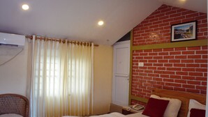 A bedroom with a bed, a chair, a window with curtains, a brick wall, and a picture on the wall. - Hotel Young's Stupa (Lekhnath)