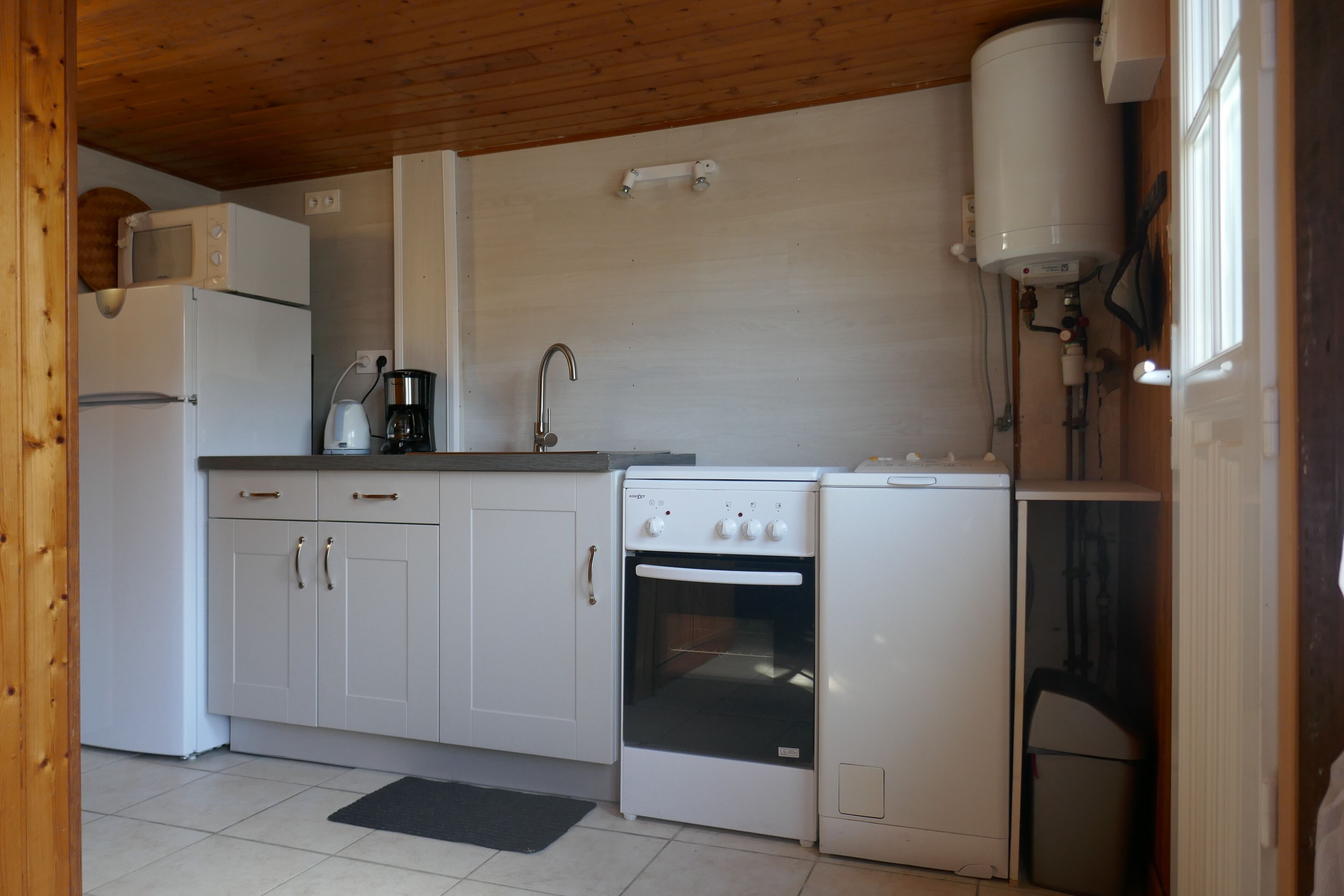 A compact kitchen with white cabinets, a built-in oven, a coffee maker, and a microwave.