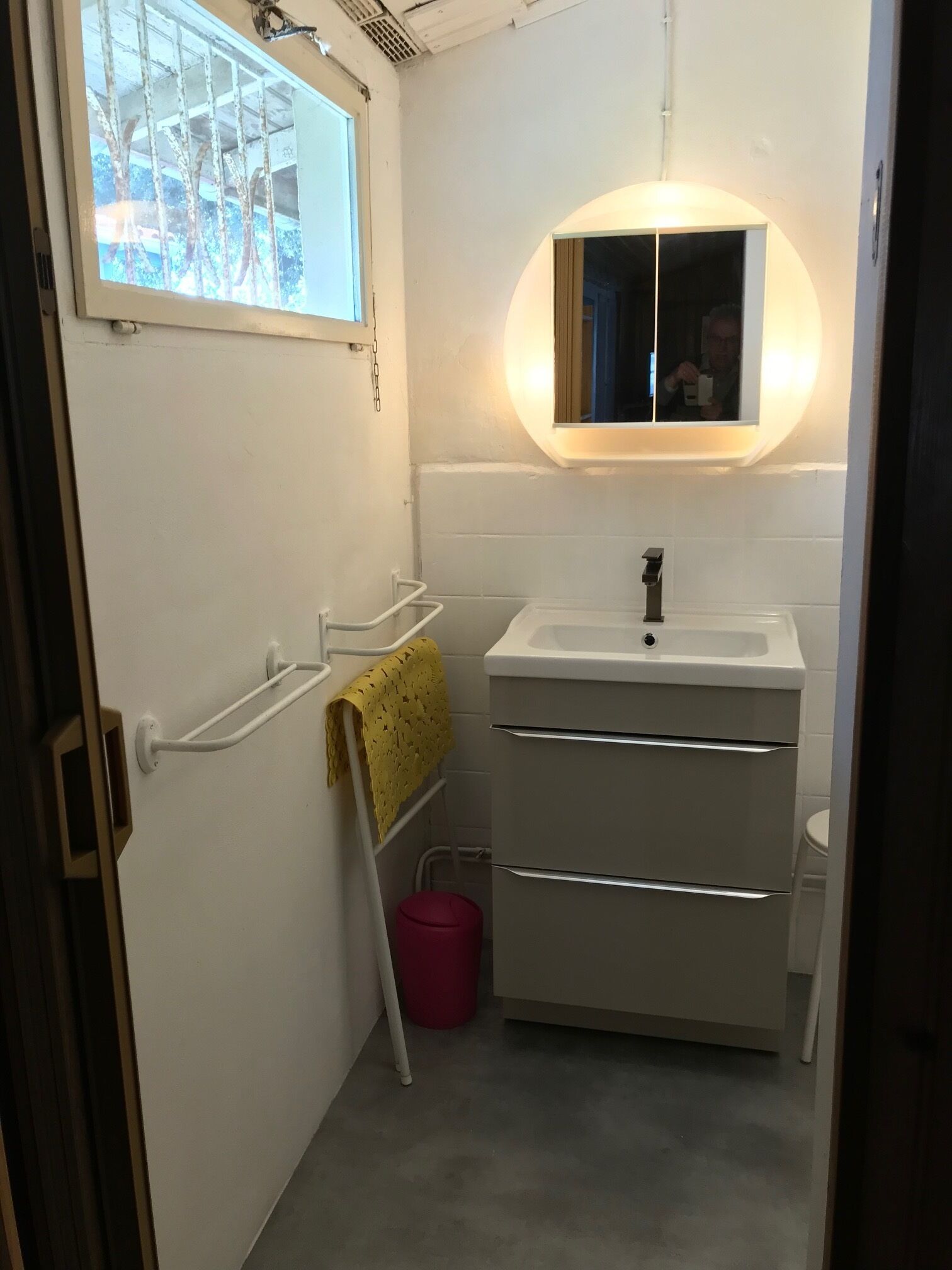 Une petite salle de bain avec un lavabo blanc, un miroir et une fenêtre située au-dessus du lavabo.