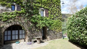 Un edificio de piedra con muros cubiertos de hiedra, un arco de piedra y una pequeña mesa de madera.