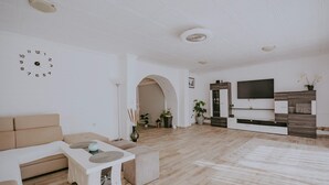 Un soggiorno moderno con un divano beige, un tavolino da caffè bianco e una TV montata su un mobile in legno.