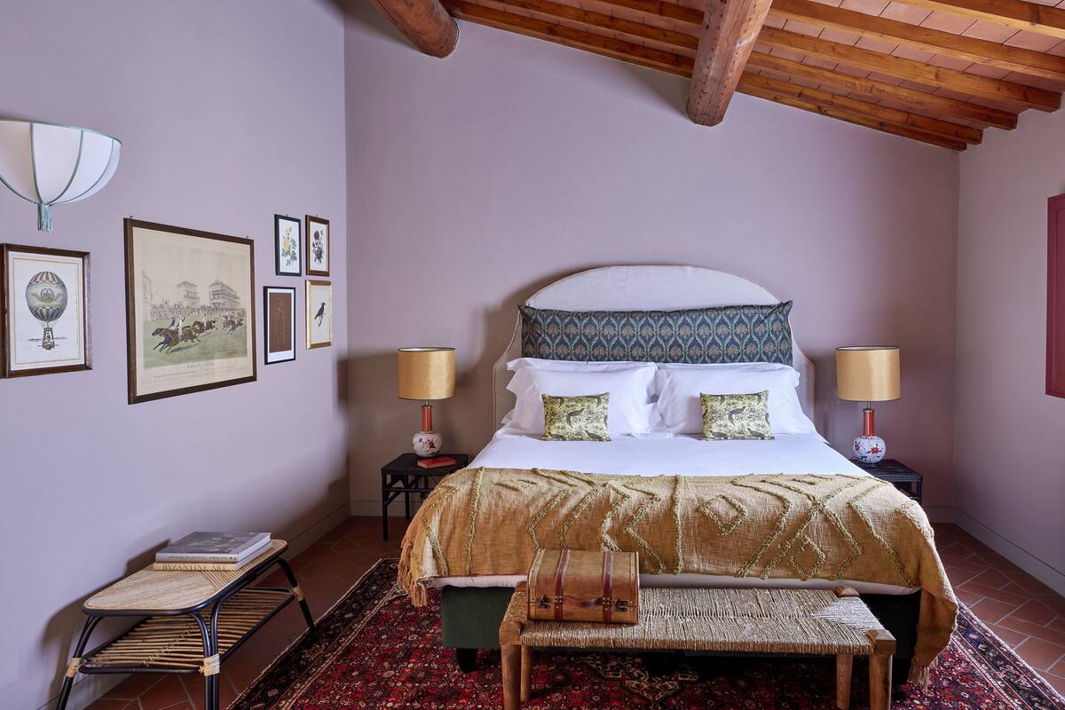 Une chambre à coucher comprenant un lit, deux tables de chevet, un banc, une chaise, un tapis et des tableaux encadrés accrochés au mur.