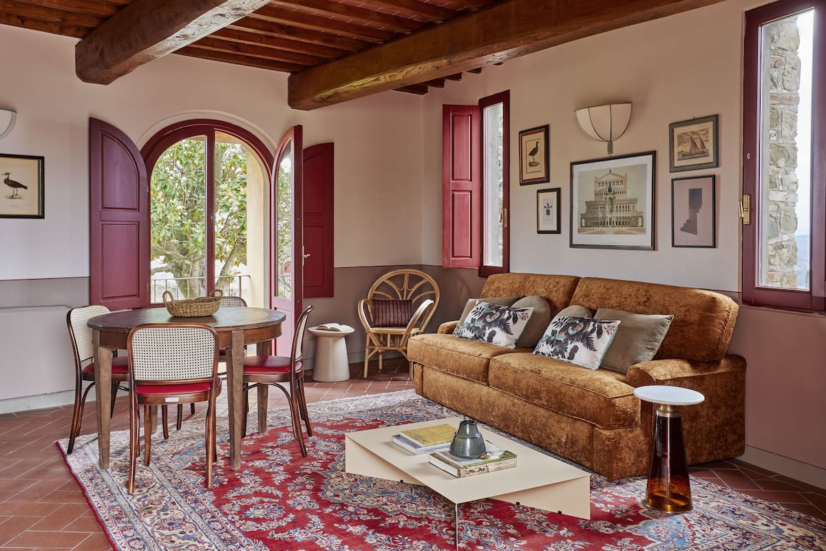 Un salon chaleureux avec un canapé marron, des fenêtres à cadre rouge et un tapis rouge à motifs.