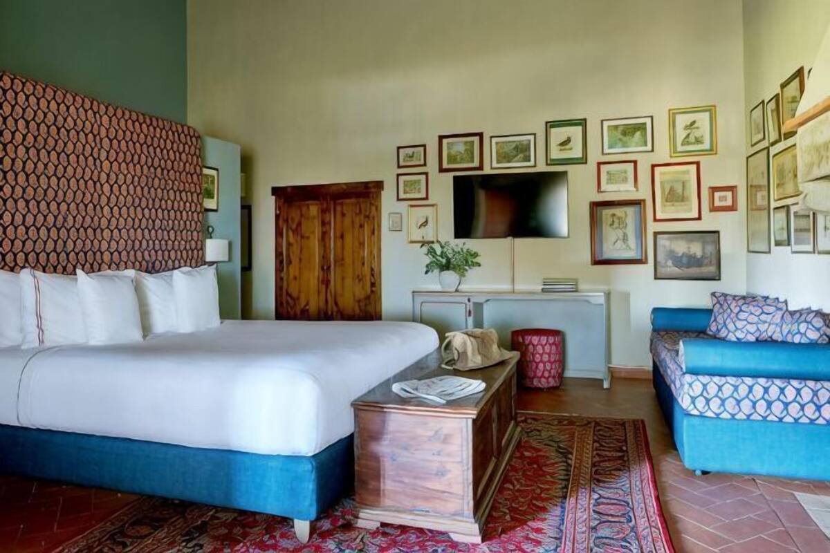 Une chambre à coucher avec un lit, un canapé bleu, une armoire en bois, une télévision et des tableaux encadrés au mur.