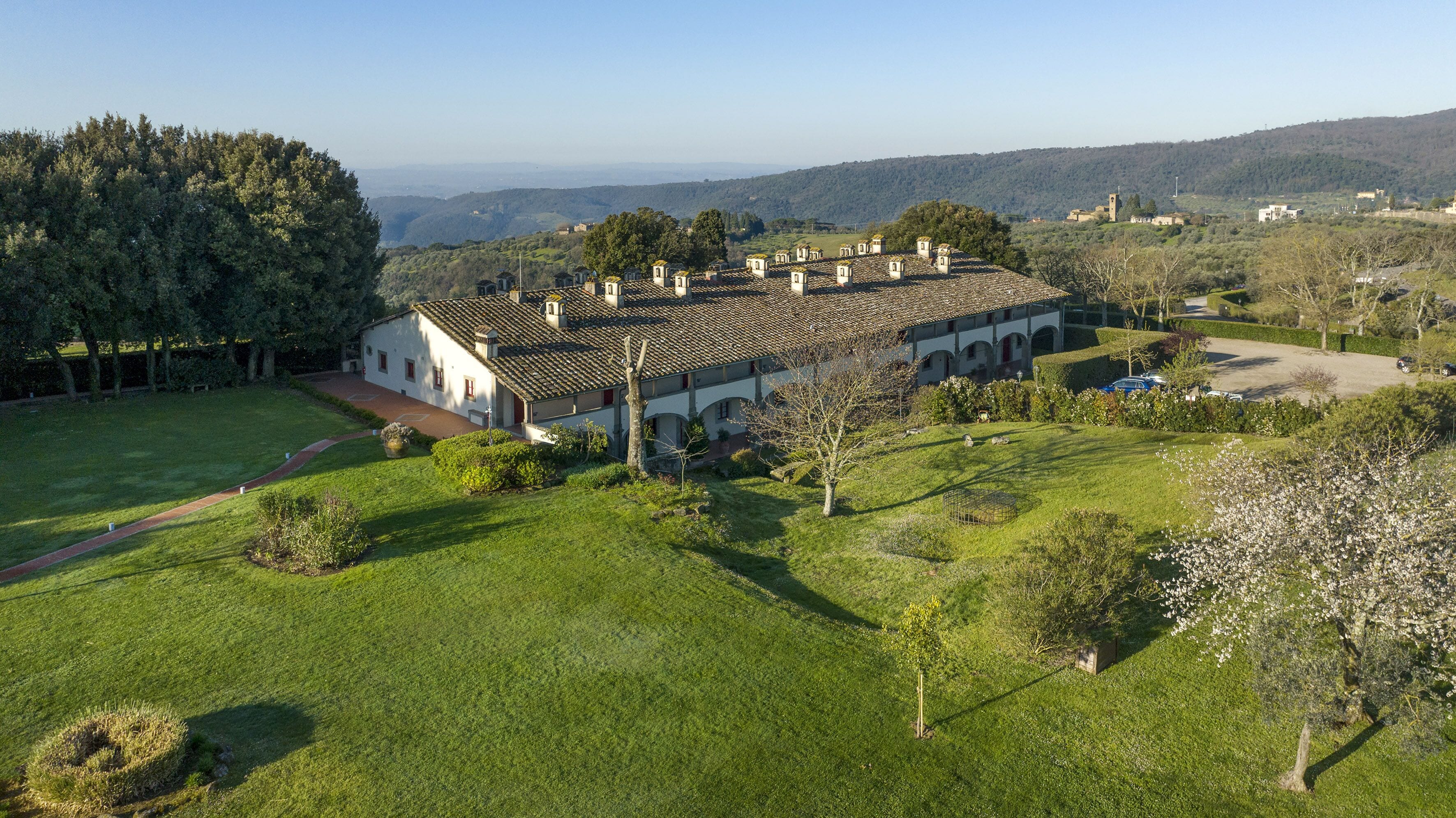 A large, white building with a tiled roof and multiple chimneys, surrounded by a well-maintained lawn and trees.