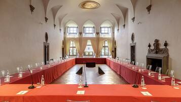 A long conference table with chairs, microphones, and water bottles, set in a room with arched ceilings and large windows.
