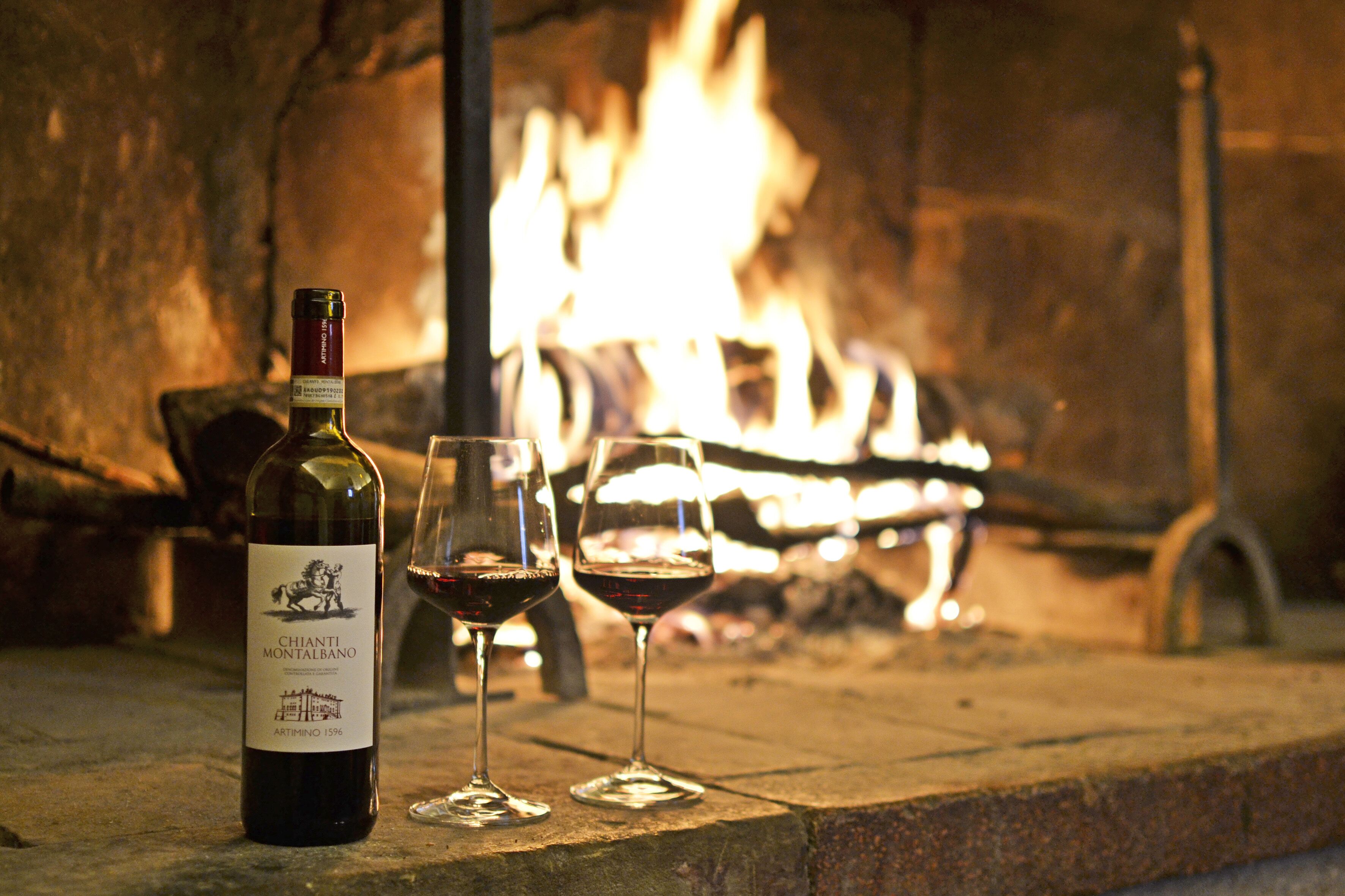 Una botella de vino Chianti Montalbano y dos copas sobre un repisa de piedra, con un fuego de fondo.