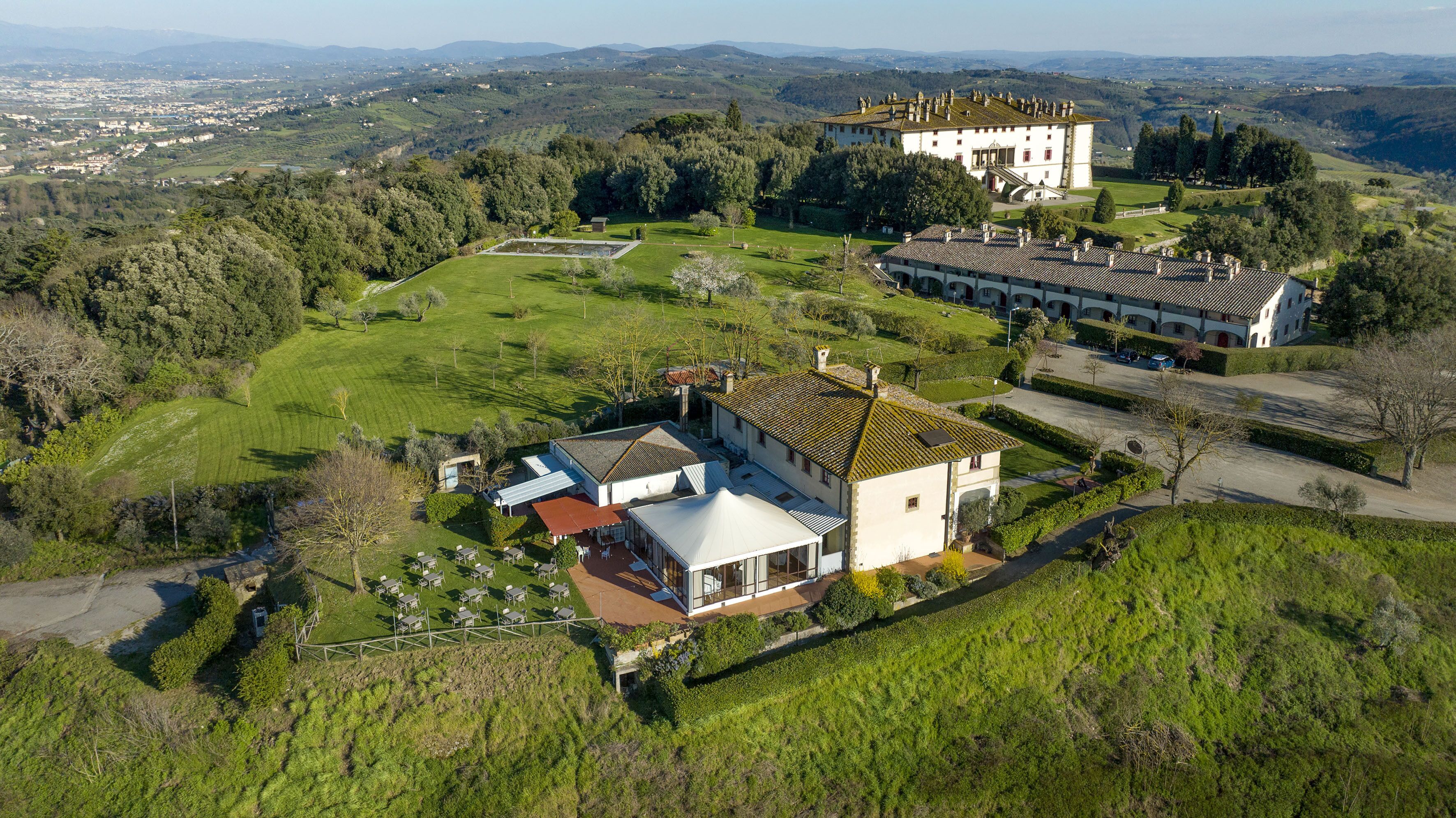 Vista aérea de una extensa propiedad con una mansión principal, un edificio más pequeño y amplios jardines verdes.