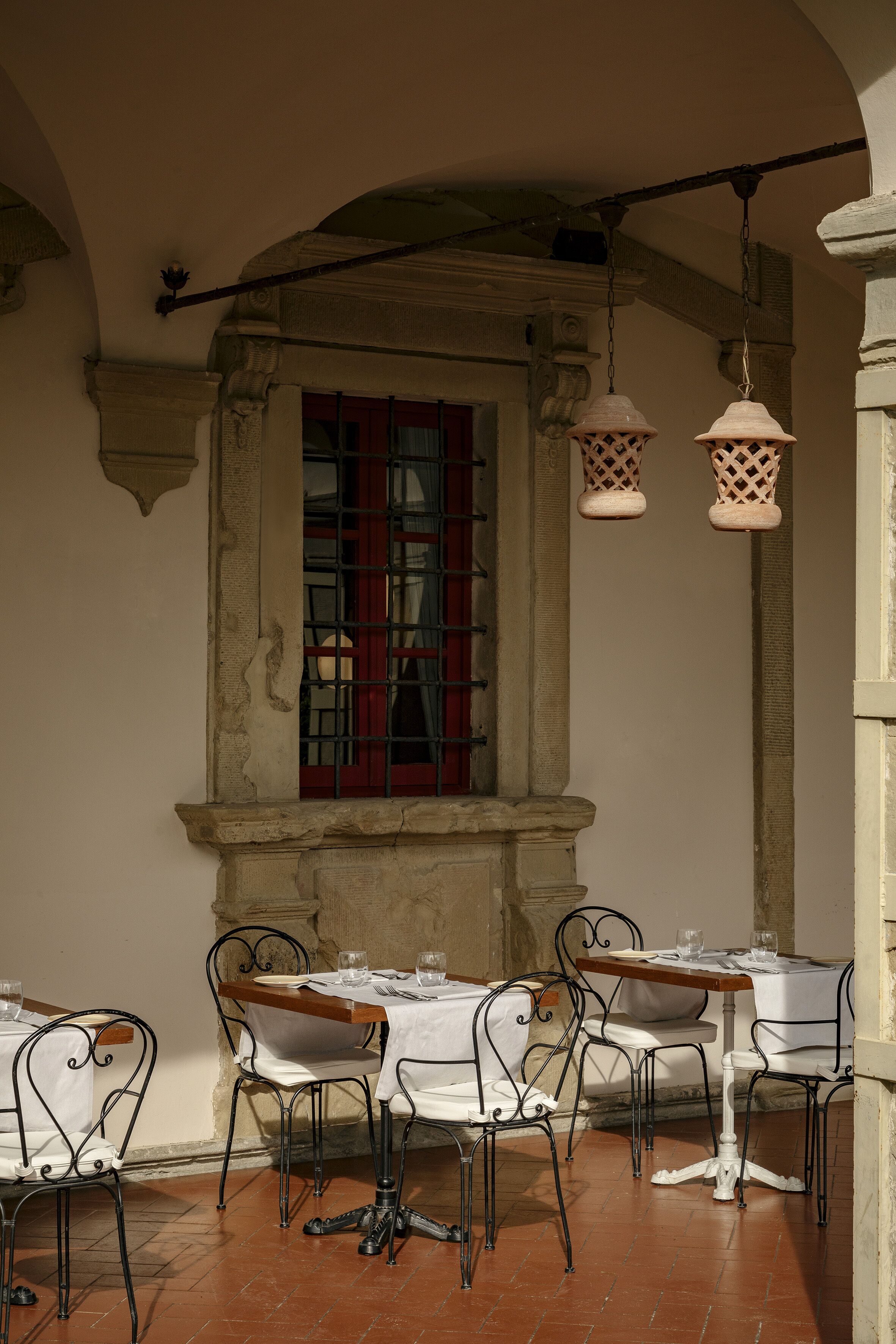 Zona pranzo con tavoli apparecchiati per due, tovaglie bianche e sedie in metallo.