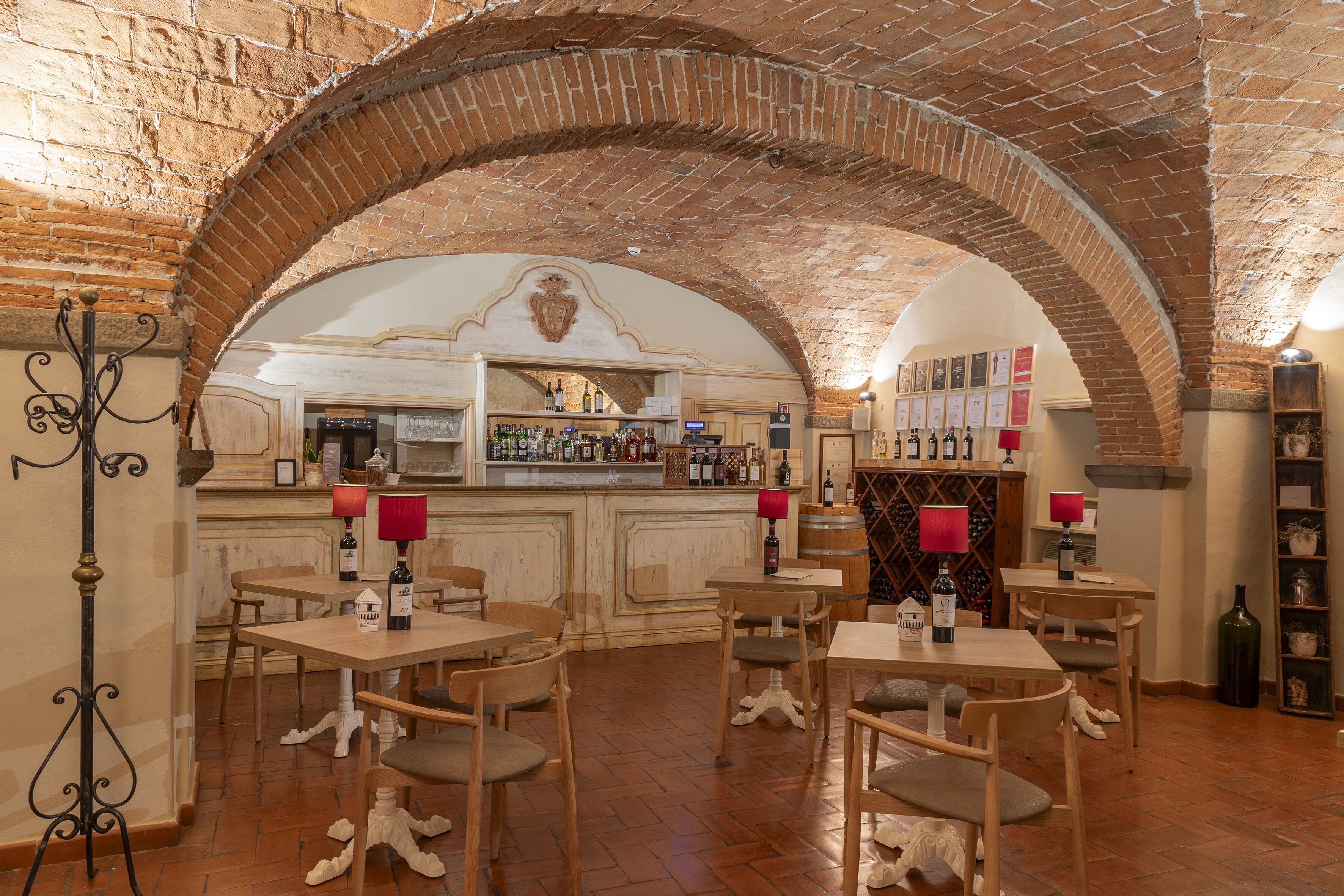 A restaurant with brick arches, wooden tables, and chairs, a bar area with bottles, and a wine rack.