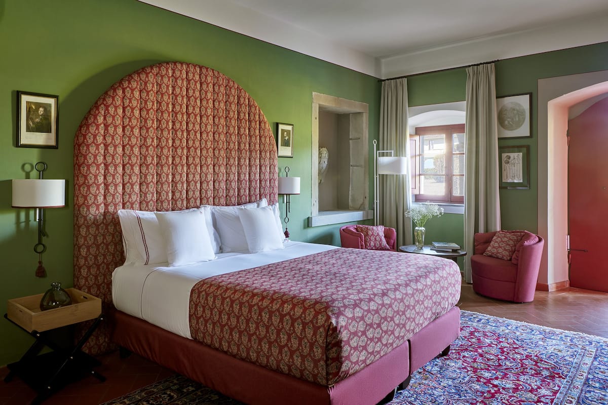 Une chambre à coucher avec un grand lit, une chaise, une table de chevet et une fenêtre.