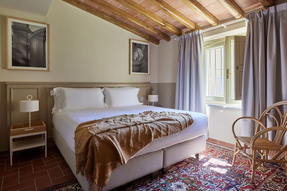 Une chambre à coucher avec un lit, une table de chevet, une chaise, une fenêtre avec des rideaux et un tapis à motifs.