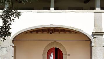 A building entrance with a red door, a bench, and a vase on the steps.