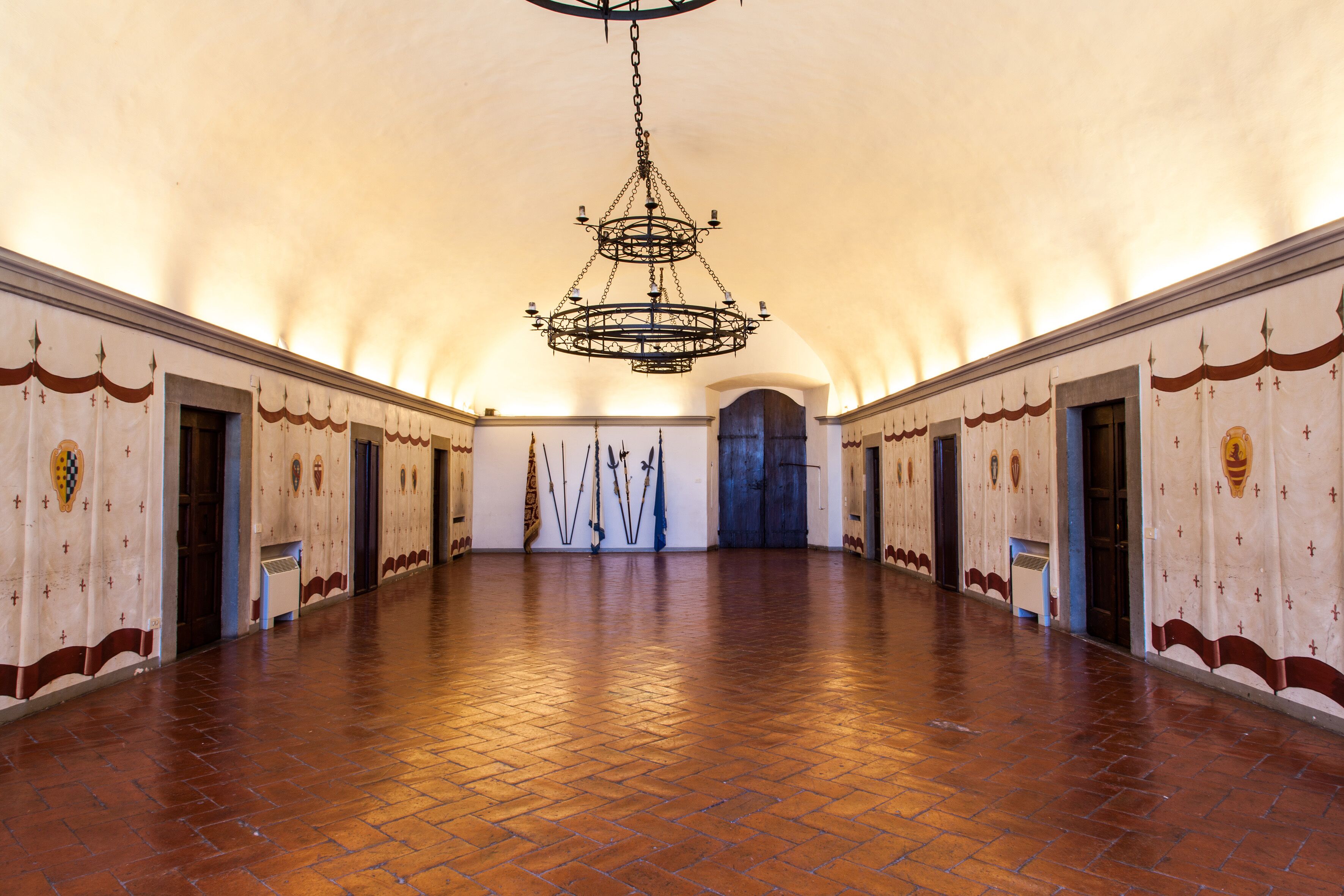 Un salón espacioso con techo alto y una gran lámpara de cristal. Las paredes están decoradas con símbolos religiosos y hay puertas que dan a habitaciones más pequeñas.