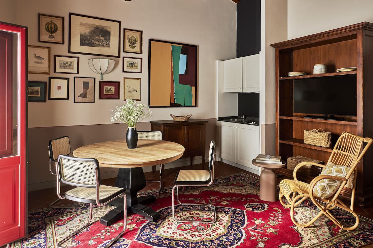 Un coin repas avec une table ronde en bois, quatre chaises, un vase de fleurs et un tapis rouge à motifs.