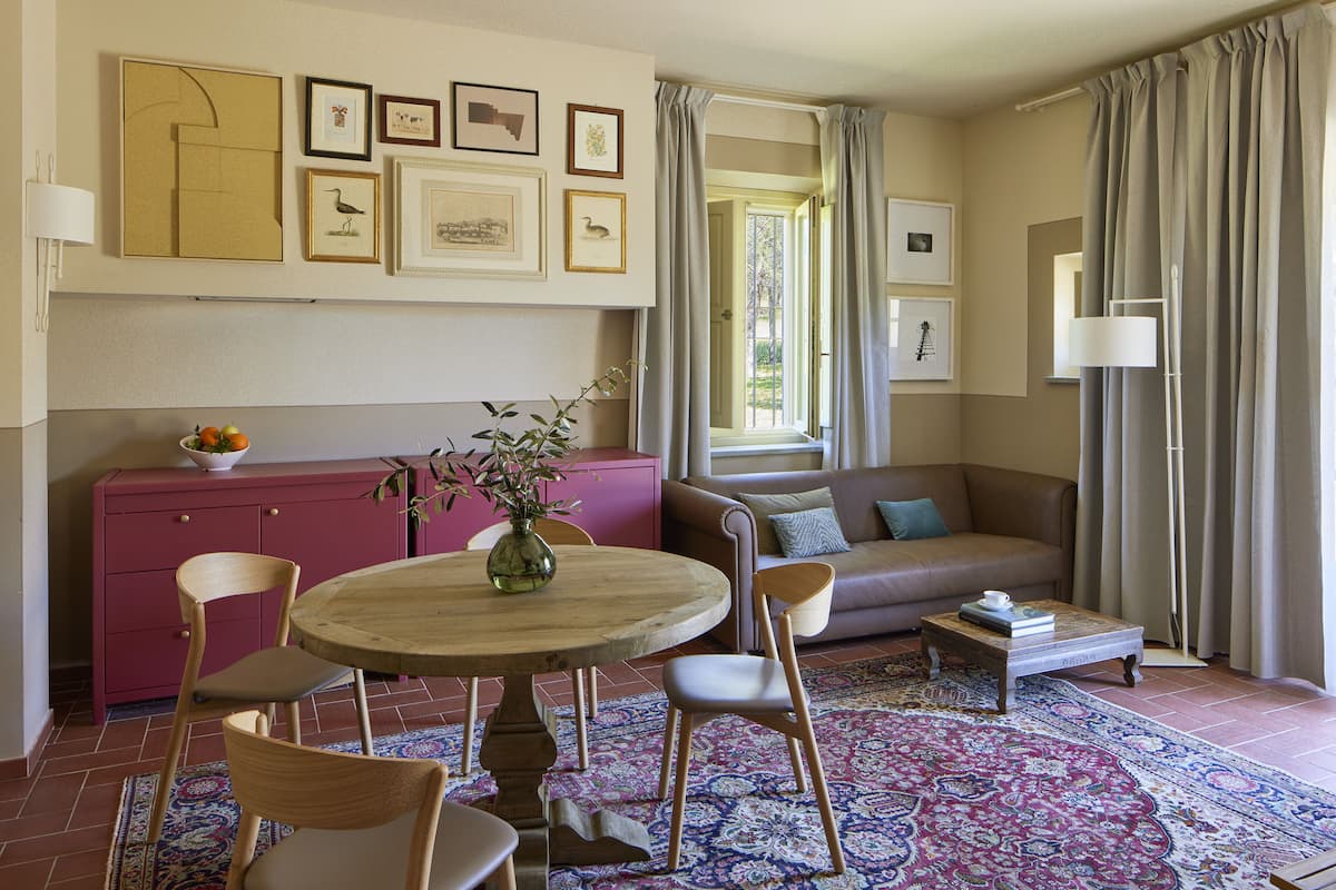 Un salon avec une table ronde en bois, des chaises, un canapé et une table basse. Des tableaux encadrés ornent le mur et un vase rempli de fleurs est posé sur la table.