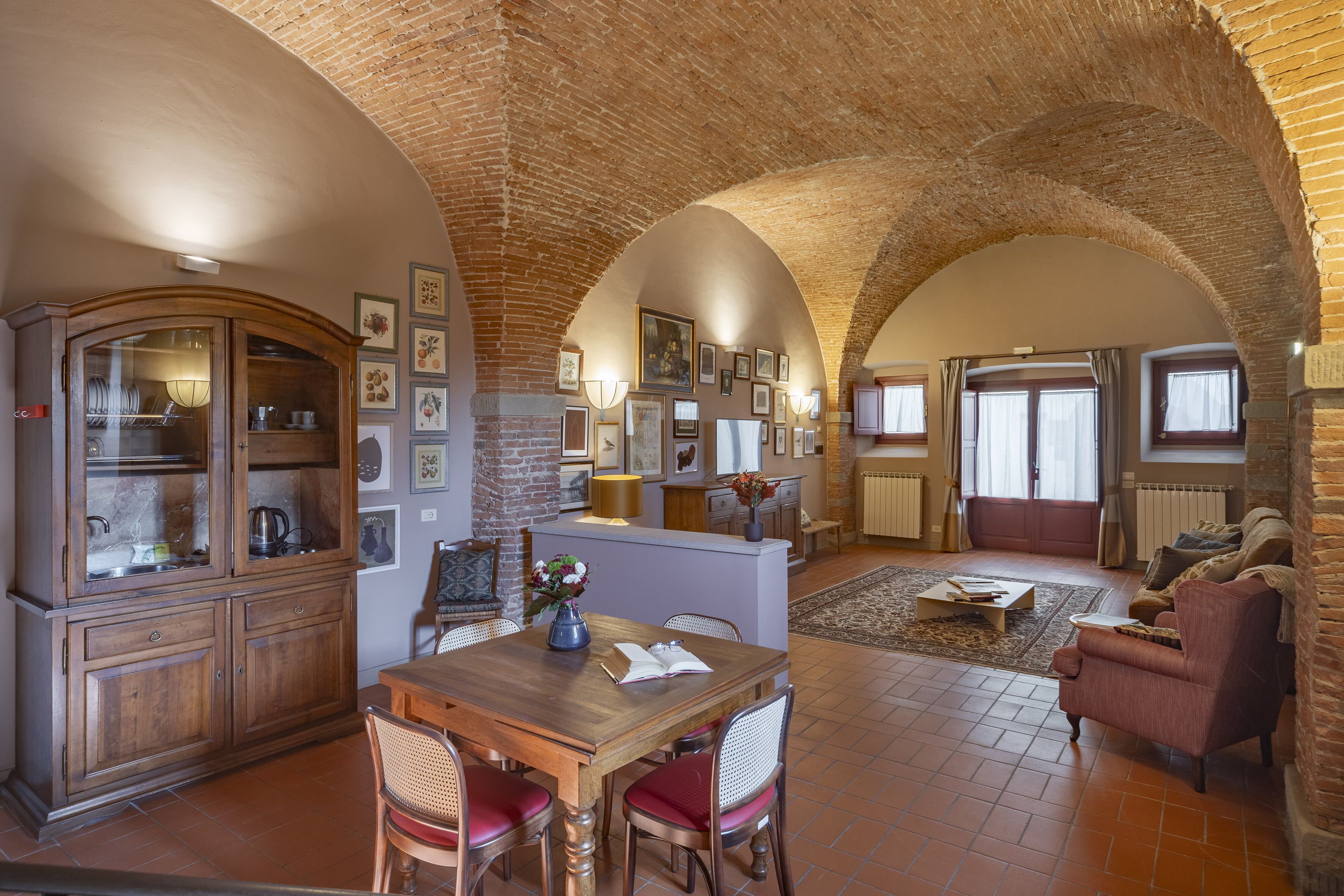 A spacious living area with a wooden dining table, red upholstered chairs, and a brick ceiling.