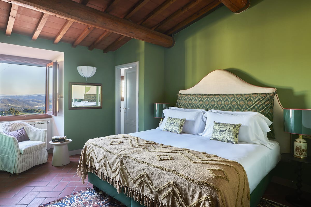 Une chambre avec un grand lit, une chaise, une petite table et une vue sur l’extérieur.