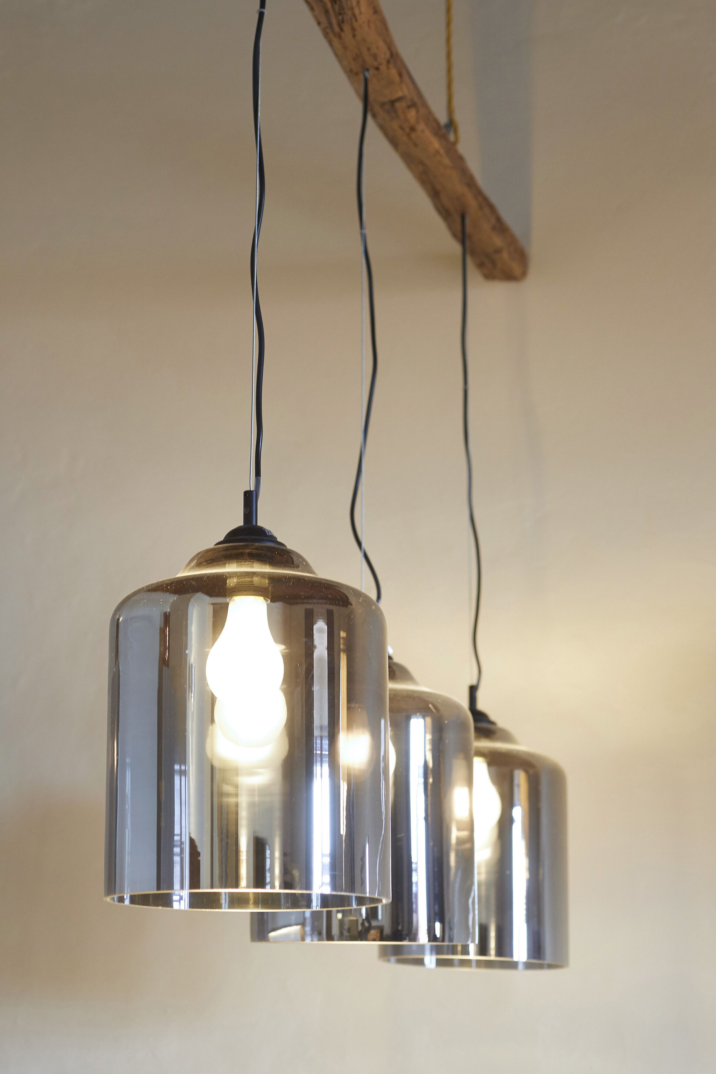 A chandelier with three light bulbs hanging from a wooden beam.