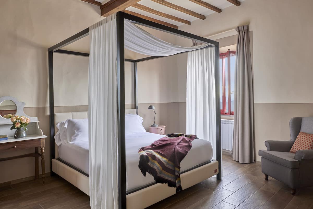 Un lit à baldaquin avec du linge de lit blanc, une table de chevet avec une lampe et une chaise avec un coussin.