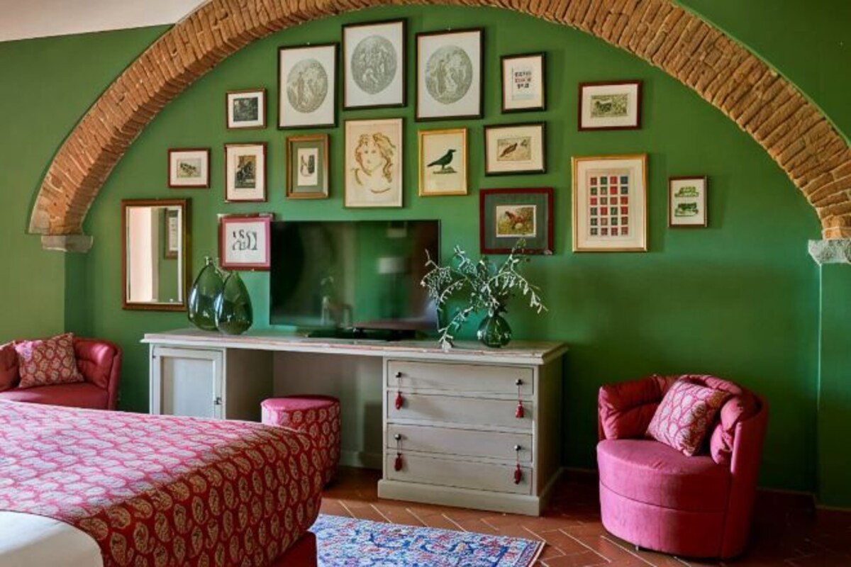 Een kamer met een groene wand, een bureau met lades, een televisie en een bed met een bedspread met een patroon.
