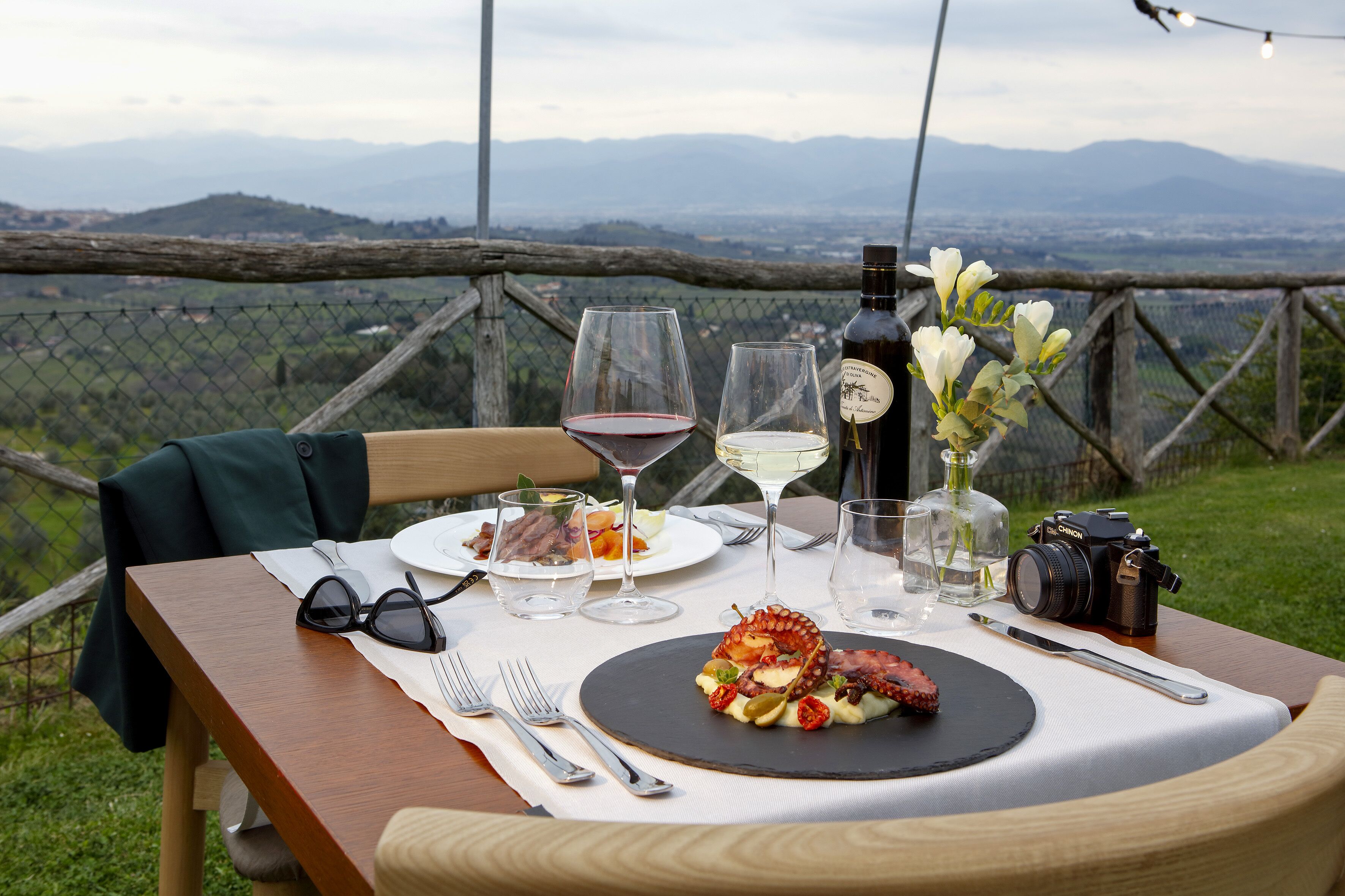 A table set for a meal with a scenic view, a camera, and a bottle of wine.