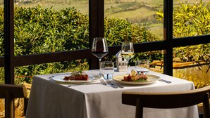Une table dressée pour deux personnes, avec vue sur un paysage montagneux grâce à de grandes fenêtres.